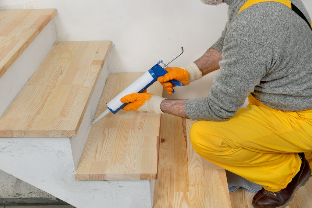 a diyer using caulk to fill in the gaps of a staircase