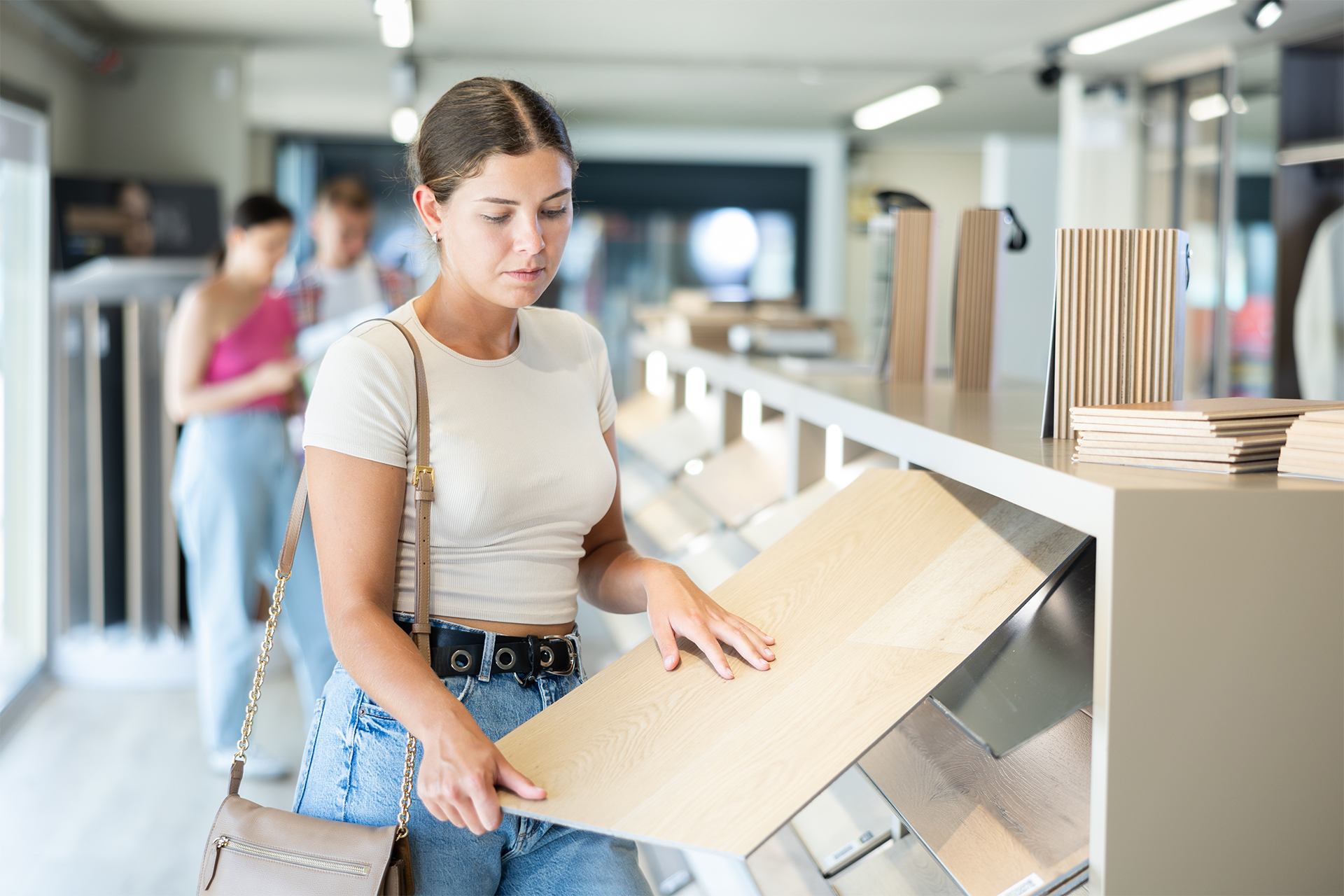 a young woman wondering how much laminate do i need while picking through samples at the flooring shop