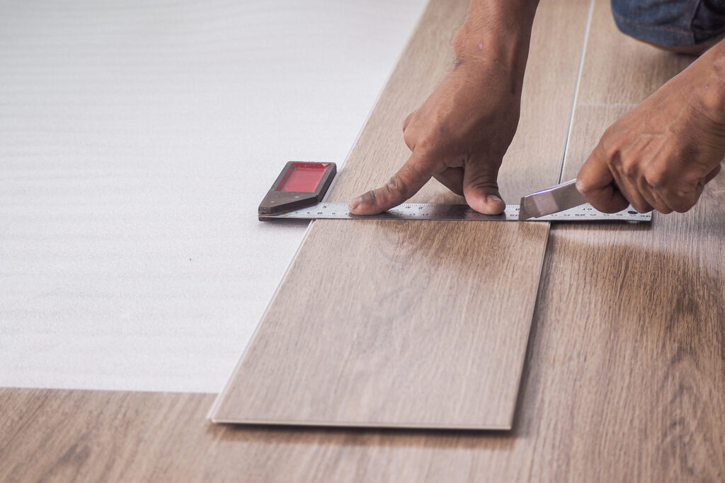 a close up of a homeowner cutting lvt flooring with a utility knife