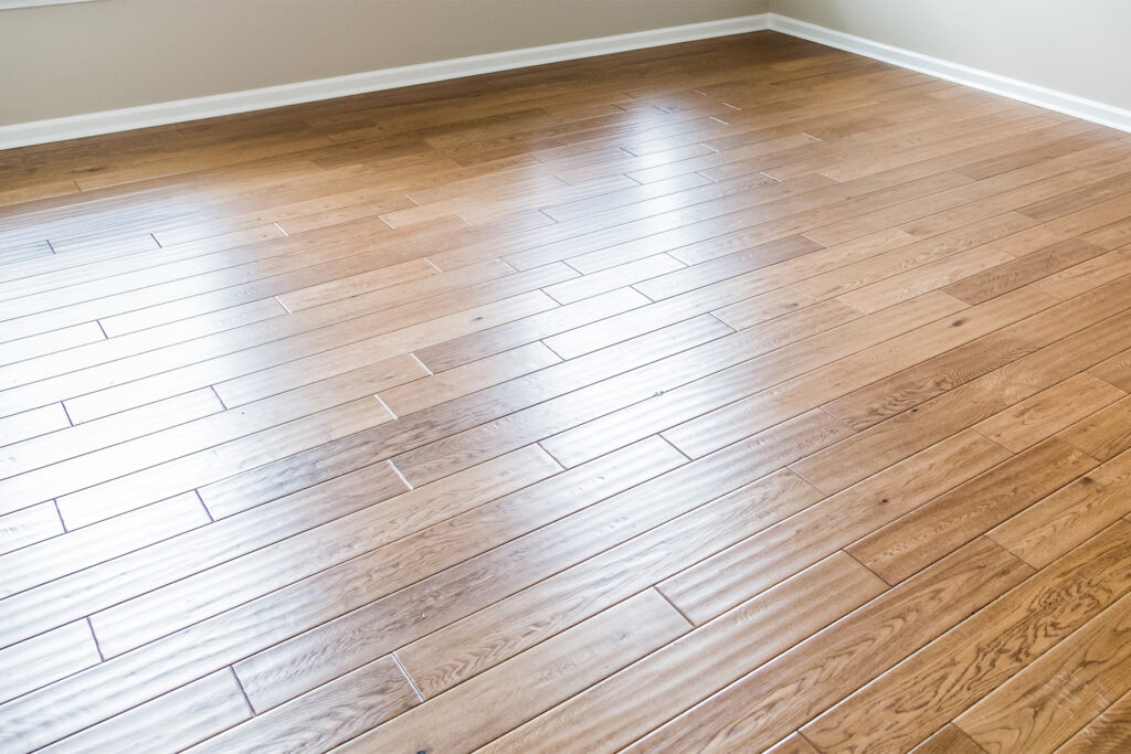 A closeup of a shiny engineered hardwood floor in an empty room.